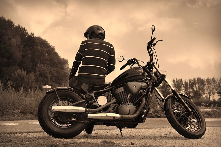 Hombre con casco sentado sobre su moto custom.